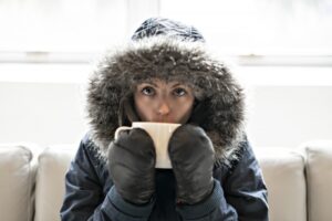 person-on-couch-with-coat-mittens-and-hot-cup-of-tea