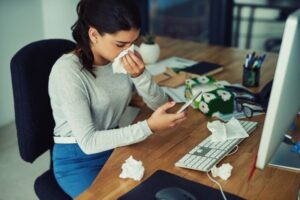 person-at-desk-trying-to-work-surrounded-by-tissues-and-blowing-nose