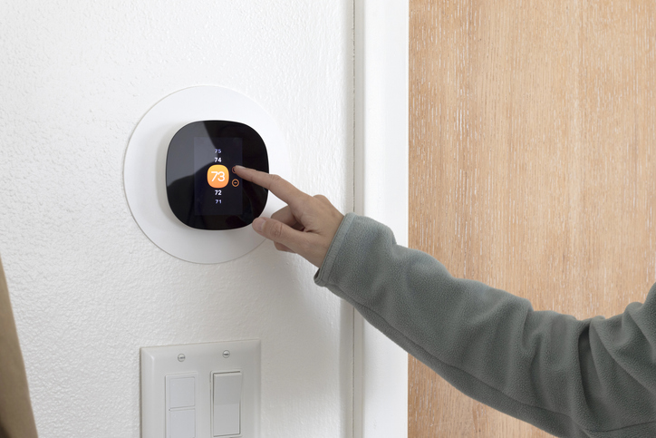 A person using a smart thermostat to increase the room temperature